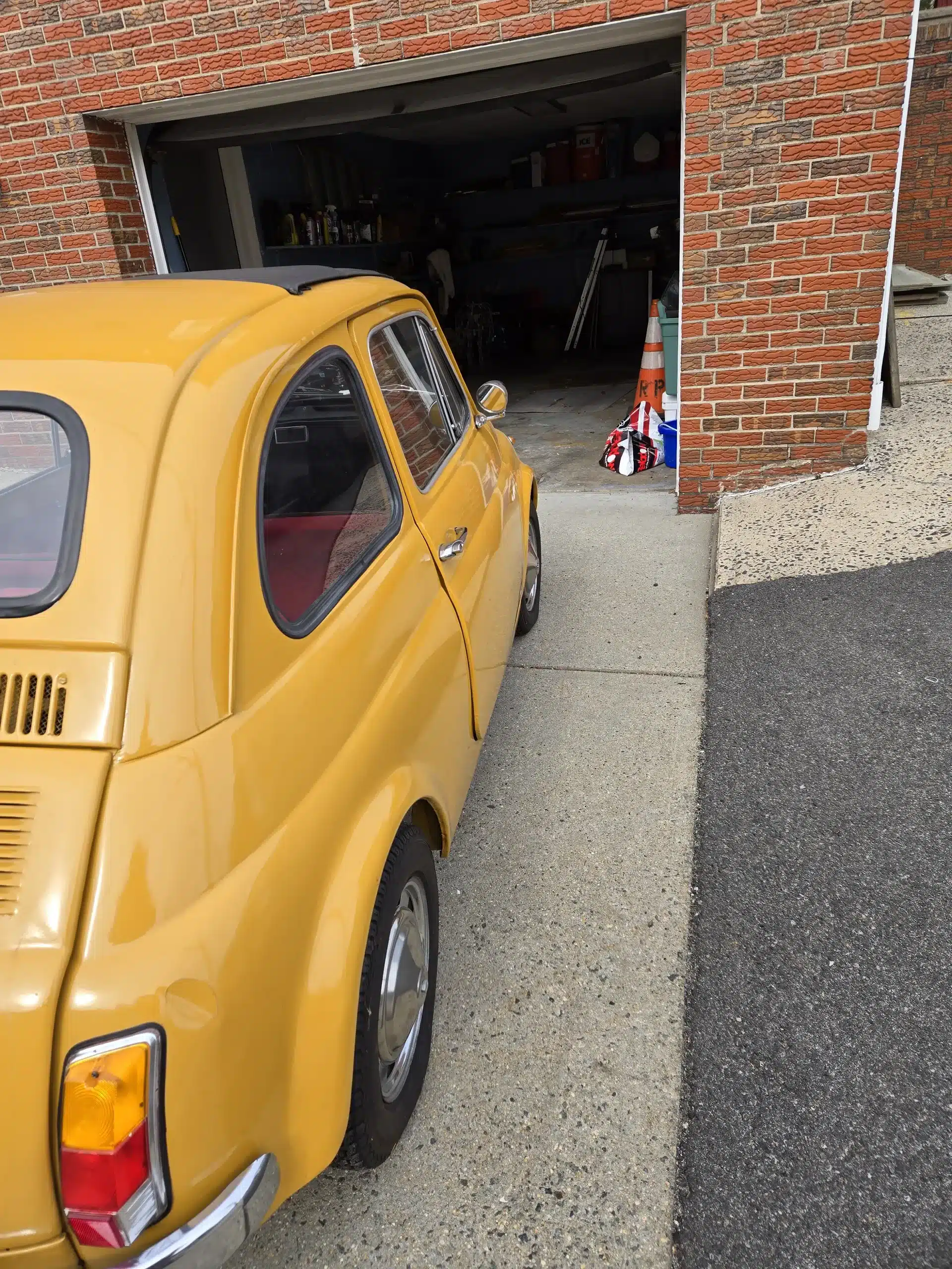 Klassischer gelber Fiat 500 von 1969 steht auf einer Einfahrt vor einer Garage mit geöffnetem Tor.