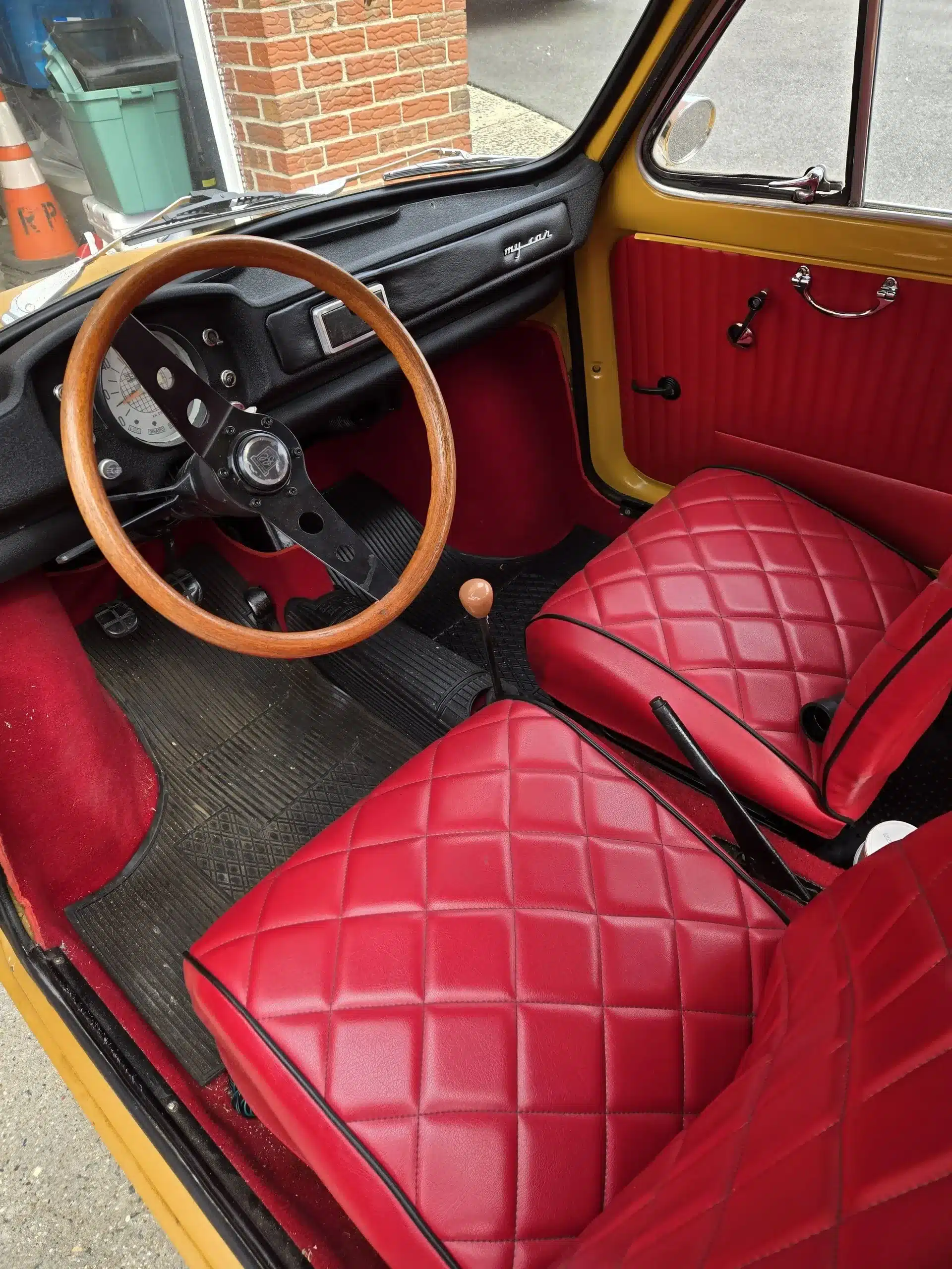Innenansicht eines Fiat 500 von 1969 mit roten Sitzpolstern und Holzlenkrad