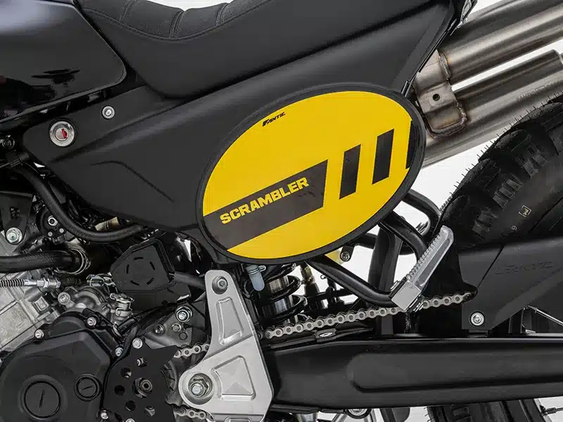 Seitliches Detail der Fantic Caballero 125 Scrambler, gelbes Designelement und Doppel-Auspuff sichtbar.