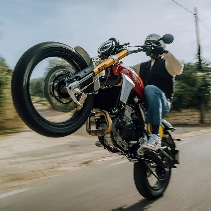 Fahrer führt mit der Fantic Caballero 500 Scrambler einen Wheelie auf einer Landstraße aus.