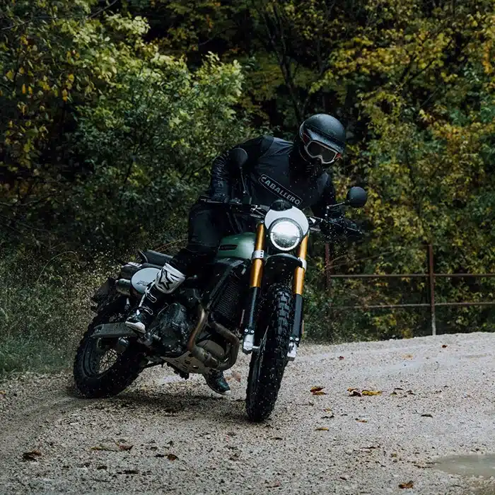 Fahrer mit Fantic Caballero 500 Scrambler auf unbefestigter Straße im Grünen