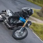 Fantic Caballero 700 Motorrad in blauer Lackierung wird von einem Fahrer sportlich in Schräglage auf einer Landstraße gefahren.
