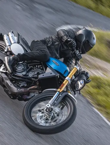 Fantic Caballero 700 Motorrad in blauer Lackierung wird von einem Fahrer sportlich in Schräglage auf einer Landstraße gefahren.