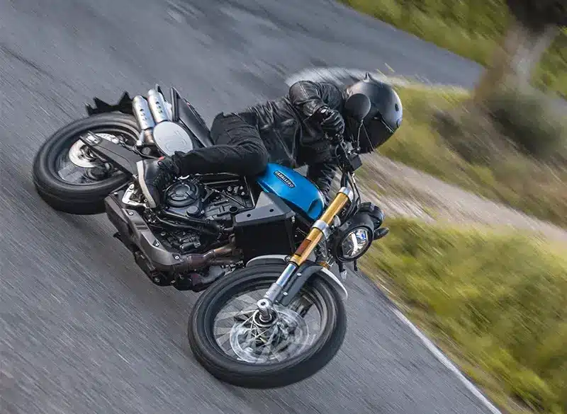 Fantic Caballero 700 Motorrad in blauer Lackierung wird von einem Fahrer sportlich in Schräglage auf einer Landstraße gefahren.