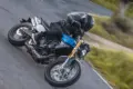 Fantic Caballero 700 Scrambler-Motorrad in Blau auf einer kurvigen Straße, Fahrer mit schwarzer Ausrüstung.