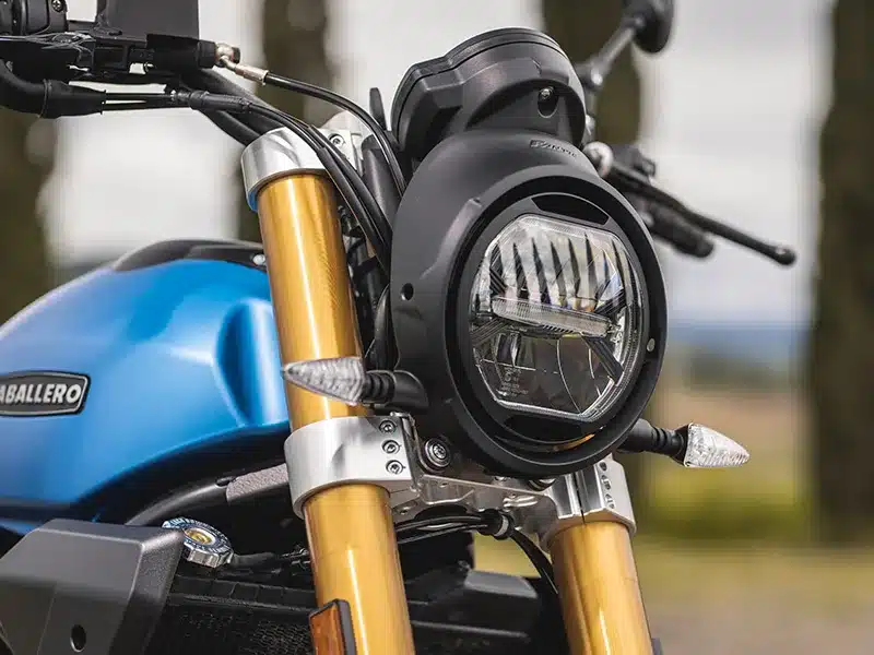 Frontdetail der Fantic Caballero 700 mit LED-Rundscheinwerfer, goldenem Fahrwerk und blauem Tank