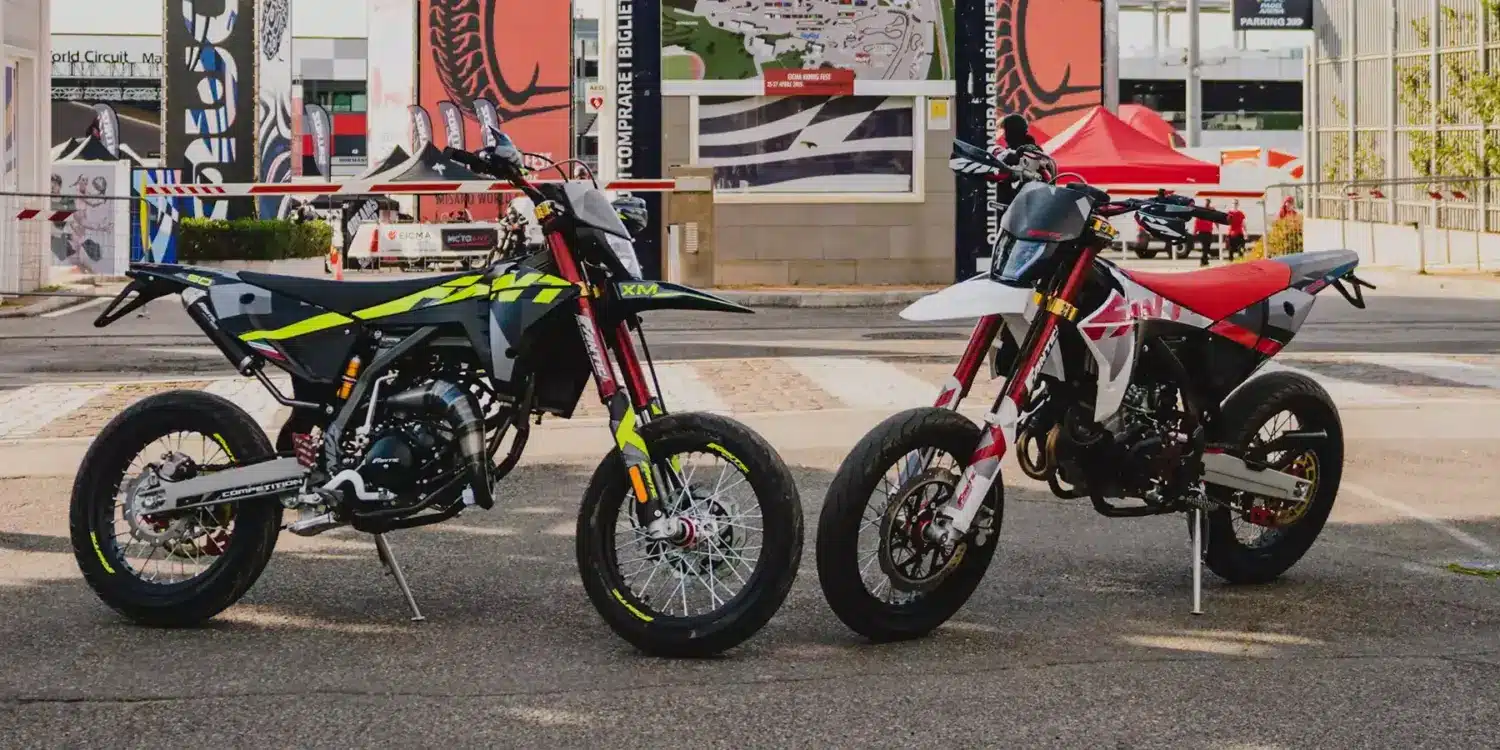 Fantic XM 50 Competition und XMF 125 Competition 2025 nebeneinander vor Messekulisse