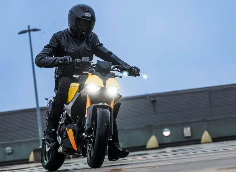 Fahrer mit Schutzkleidung fährt eine Fantic Stealth 125 in gelber Lackierung auf feuchtem Beton