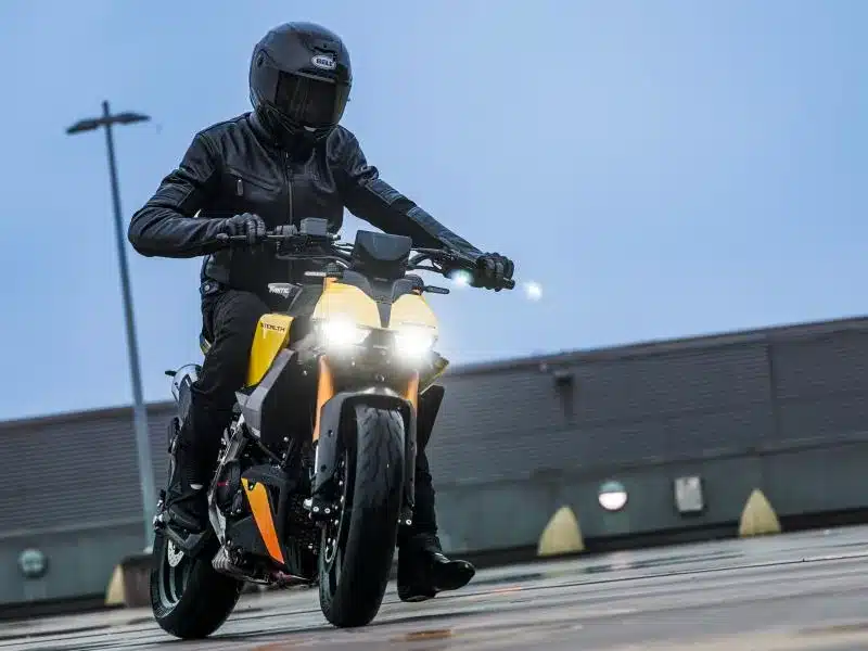 Fahrer mit Schutzkleidung fährt eine Fantic Stealth 125 in gelber Lackierung auf feuchtem Beton