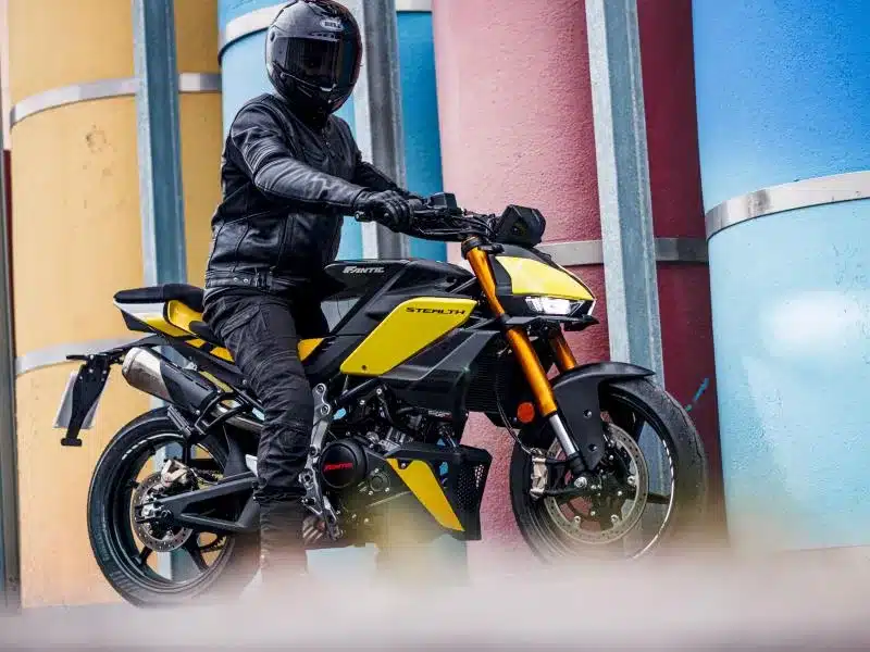 Motorradfahrer auf einer Fantic Stealth 125 in Gelb vor bunten Betonpfeilern