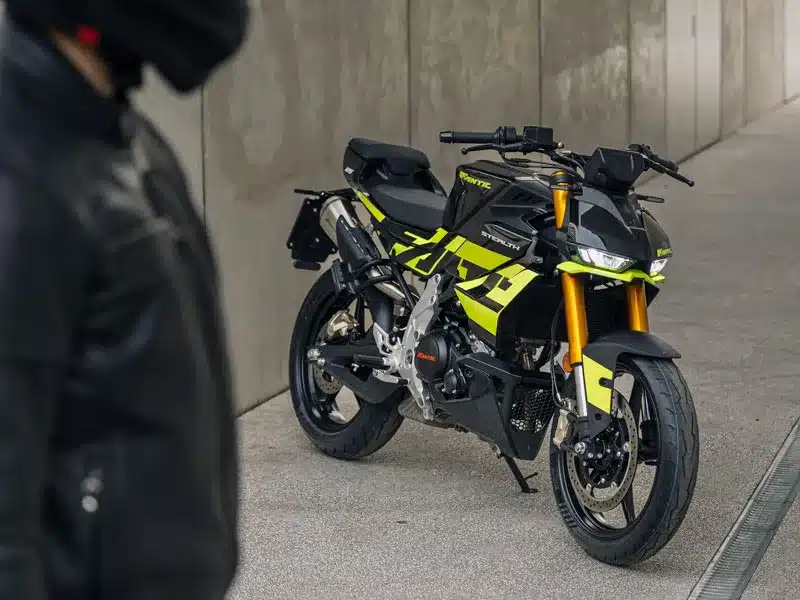 Fantic Stealth 125 in Acid Green, abgestellt neben einer Betonwand, im Vordergrund eine Person mit Motorradjacke
