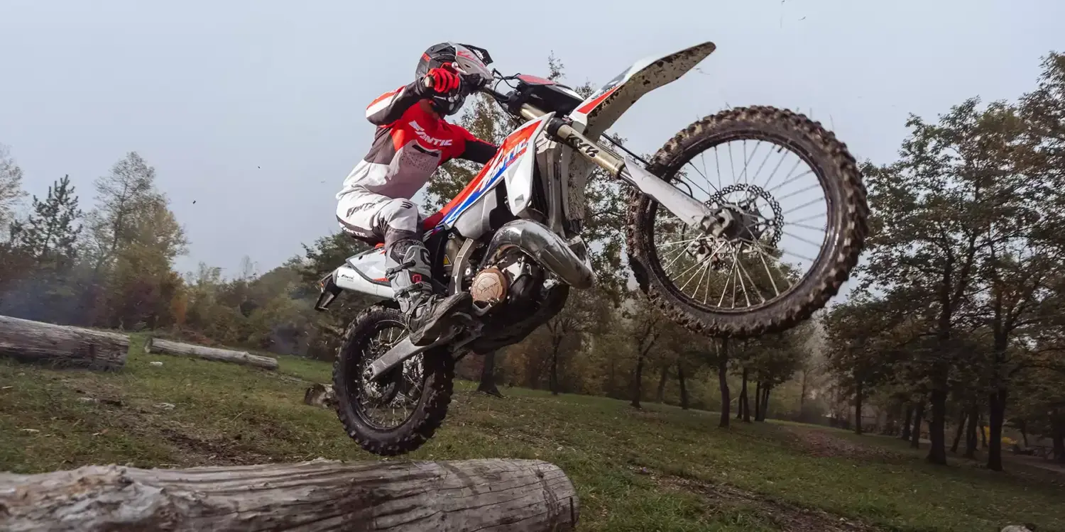 Fantic XE 300 Enduro-Motorrad Modelljahr 2026 im Offroad-Einsatz, fährt über einen Baumstamm im Gelände.