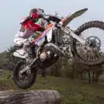 Fantic XE 300 Enduro-Motorrad Modelljahr 2026 im Offroad-Einsatz, fährt über einen Baumstamm im Gelände.