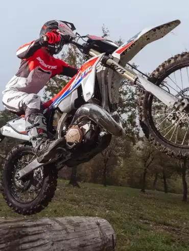 Fantic XE 300 Enduro-Motorrad Modelljahr 2026 im Offroad-Einsatz, fährt über einen Baumstamm im Gelände.