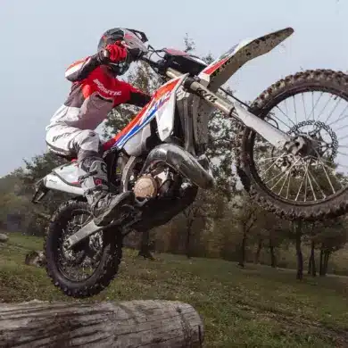 Fantic XE 300 Enduro-Motorrad Modelljahr 2026 im Offroad-Einsatz, fährt über einen Baumstamm im Gelände.