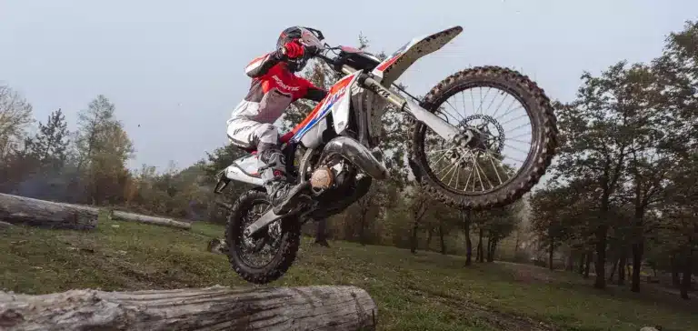 Fantic XE 300 Enduro-Motorrad Modelljahr 2026 im Offroad-Einsatz, fährt über einen Baumstamm im Gelände.