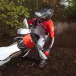 Fantic XEF 310 Enduro-Motorrad fährt durch bewaldetes Gelände, gesteuert von einem Fahrer in roter Ausrüstung.