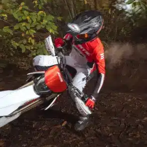 Fantic XEF 310 Enduro-Motorrad fährt durch bewaldetes Gelände, gesteuert von einem Fahrer in roter Ausrüstung.