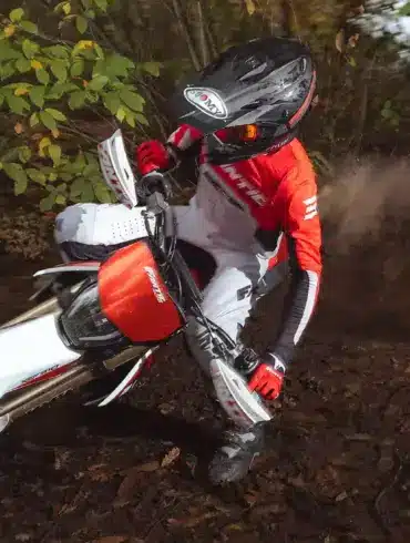 Fantic XEF 310 Enduro-Motorrad fährt durch bewaldetes Gelände, gesteuert von einem Fahrer in roter Ausrüstung.