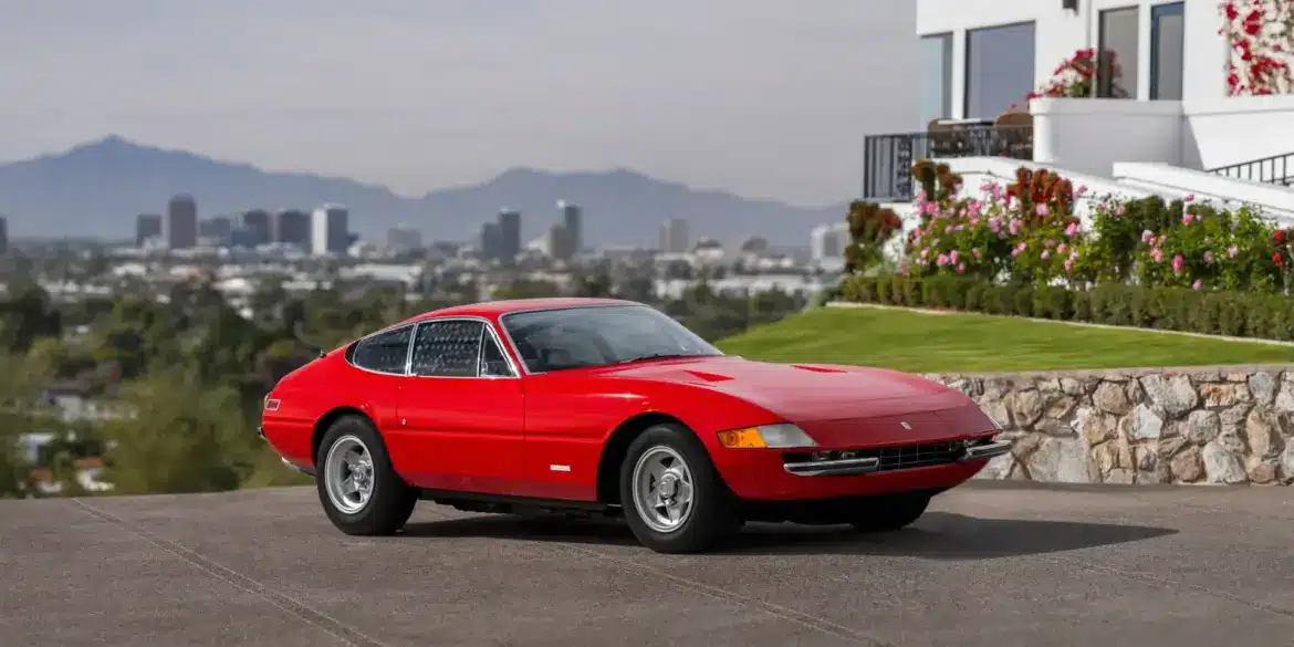 Ferrari 365 GTB/4 Daytona Berlinetta von 1970 in Rot, seitlich fotografiert vor einer Stadtansicht und einem modernen Haus.