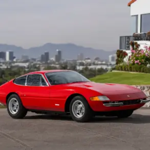Ferrari 365 GTB/4 Daytona Berlinetta von 1970 in Rot, seitlich fotografiert vor einer Stadtansicht und einem modernen Haus.