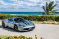 Ferrari 458 Speciale in silbergrau mit schwarzen Streifen, geparkt vor Palmen und türkisblauem Meer
