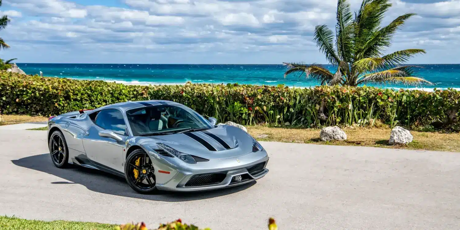 Ferrari 458 Speciale in silbergrau mit schwarzen Streifen, geparkt vor Palmen und türkisblauem Meer