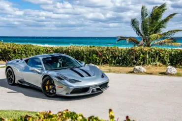 Ferrari 458 Speciale in silbergrau mit schwarzen Streifen, geparkt vor Palmen und türkisblauem Meer