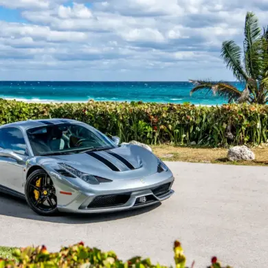 Ferrari 458 Speciale in silbergrau mit schwarzen Streifen, geparkt vor Palmen und türkisblauem Meer