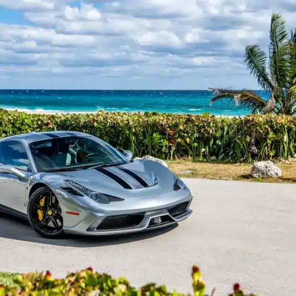 Ferrari 458 Speciale in silbergrau mit schwarzen Streifen, geparkt vor Palmen und türkisblauem Meer