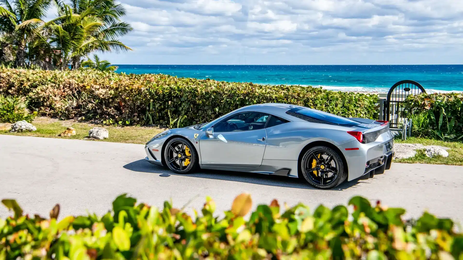 Silberner Ferrari 458 Speciale mit schwarzen Rädern und gelben Bremssätteln vor einer Küstenlandschaft