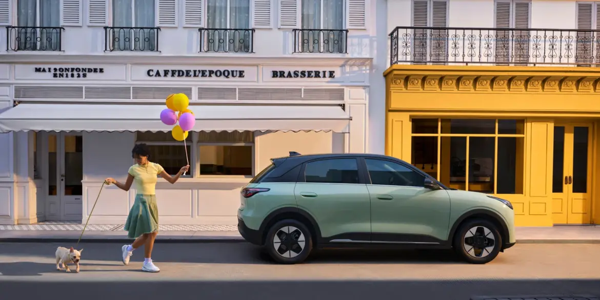 Geely EX2 Elektroauto geparkt in einer Stadt, Frau mit Hund und Luftballons spaziert vorbei
