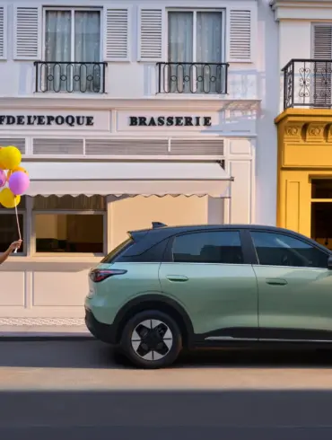 Geely EX2 Elektroauto geparkt in einer Stadt, Frau mit Hund und Luftballons spaziert vorbei