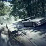 Genesis Electrified G80 als elektrische Limousine auf einer sonnigen, bewaldeten Straße in dynamischer Fahrt.