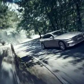 Genesis Electrified G80 als elektrische Limousine auf einer sonnigen, bewaldeten Straße in dynamischer Fahrt.