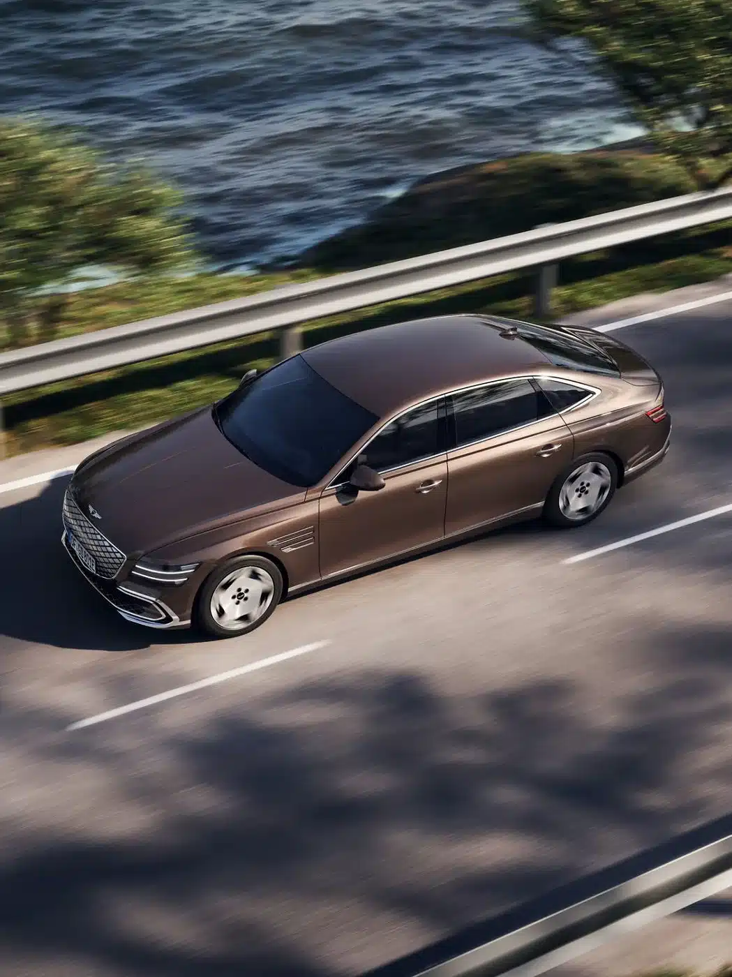 Genesis Electrified G80 elektrische Luxuslimousine fährt auf einer Straße am Wasser entlang.