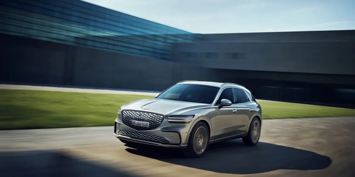 Genesis Electrified GV70 fährt dynamisch vor moderner Kulisse.