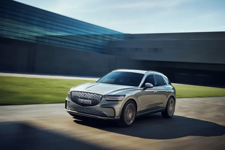Genesis Electrified GV70 fährt dynamisch vor moderner Kulisse.