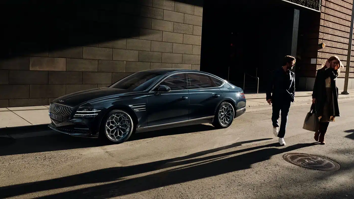 Genesis G80 Limousine steht am Straßenrand neben zwei Personen bei Tageslicht.