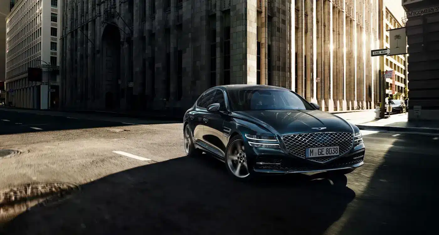 Genesis G80 Limousine fährt auf einer sonnigen Straße in der Stadt, frontal aufgenommen