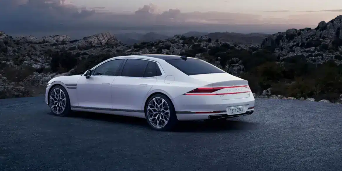 Weißer Genesis G90 von hinten auf einer Straße, umgeben von Bergen und bewölktem Himmel