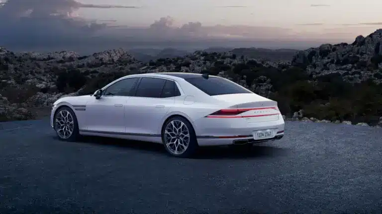 Weißer Genesis G90 von hinten auf einer Straße, umgeben von Bergen und bewölktem Himmel