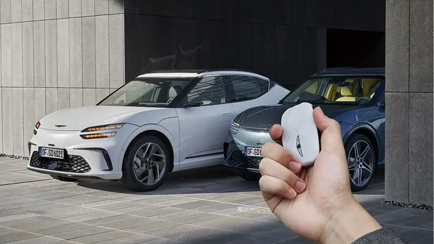 Zwei Genesis GV60 Fahrzeuge, einer weiß und einer grau, vor einem Gebäude, im Vordergrund ein Hand mit Fahrzeugschlüssel.