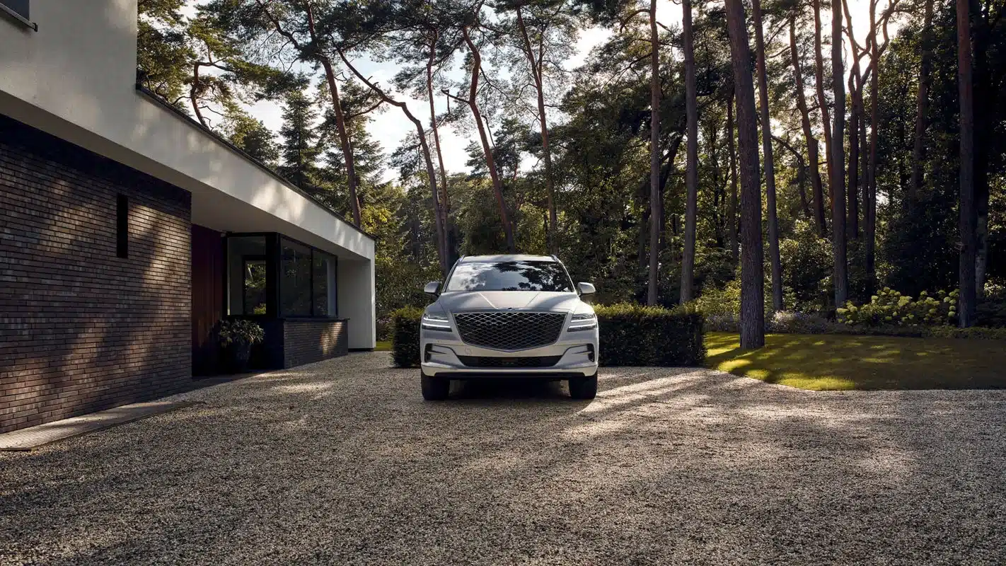 Genesis GV80 SUV vor einem modernen Haus mit Wald im Hintergrund.