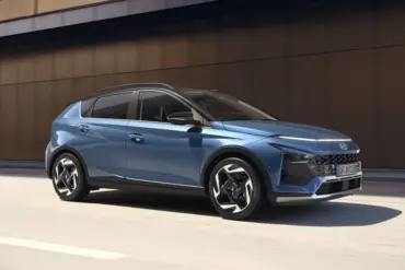 Blauer Hyundai BAYON fährt auf einer Straße entlang einer modernen Gebäudefassade