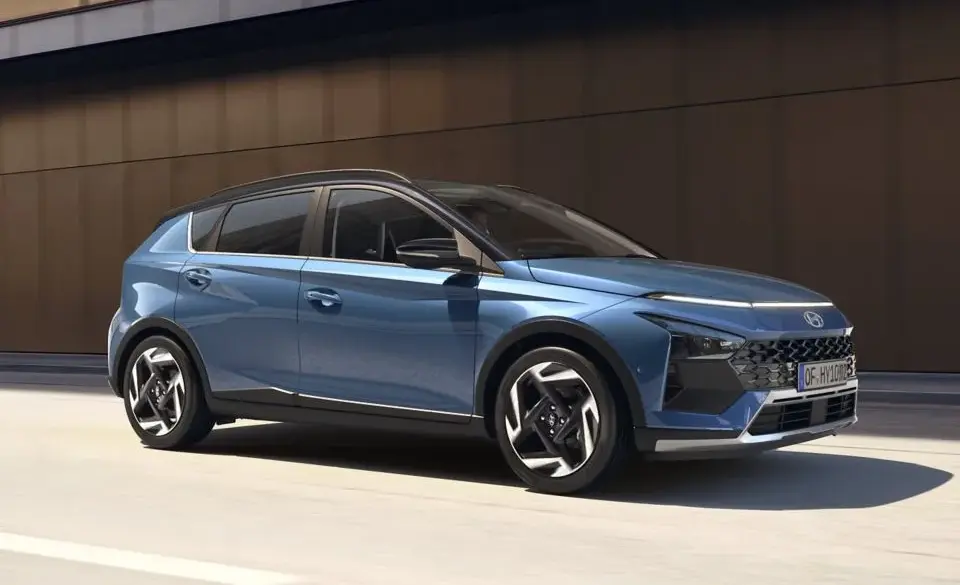 Blauer Hyundai BAYON fährt auf einer Straße entlang einer modernen Gebäudefassade