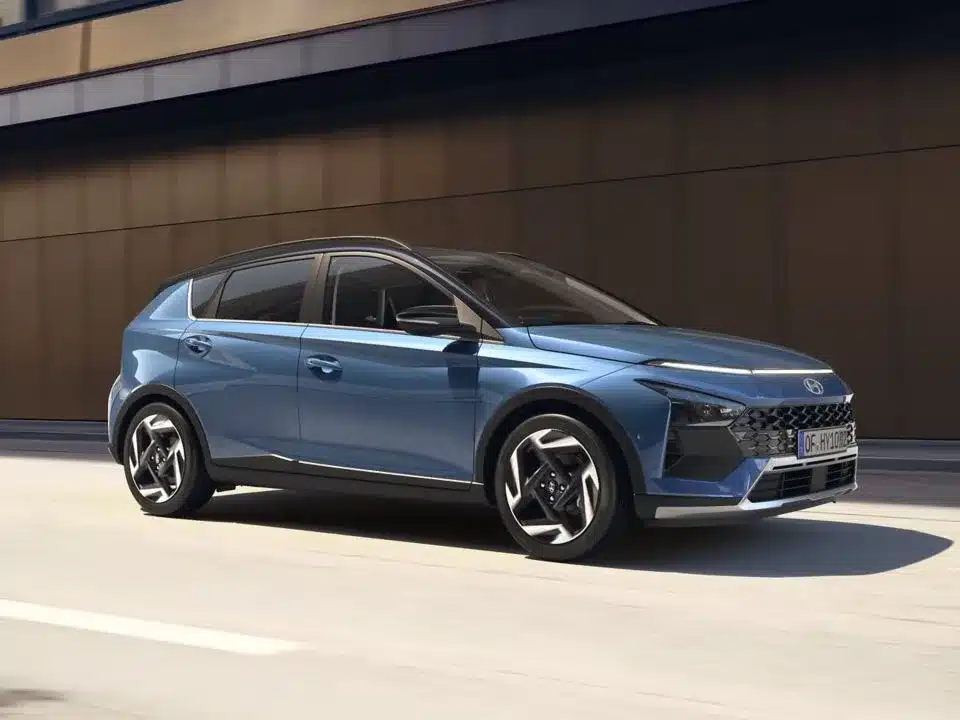 Blauer Hyundai BAYON fährt auf einer Straße entlang einer modernen Gebäudefassade