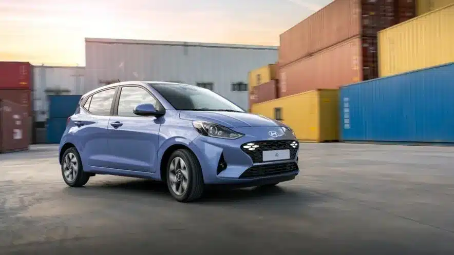 Hyundai i10 in hellblauer Farbe vor bunten Containern auf einem Industriegelände