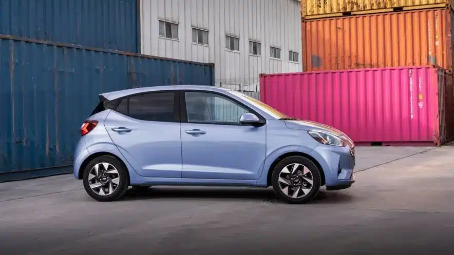Ein blauer Hyundai i10 steht seitlich vor bunten Containern und unterstreicht sein stadttaugliches Design.