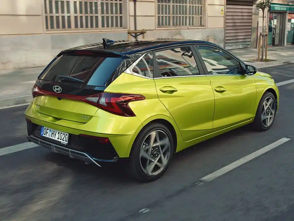 Heckansicht eines gelbgrünen Hyundai i20 auf einer Stadtstraße, dynamisch in Bewegung.